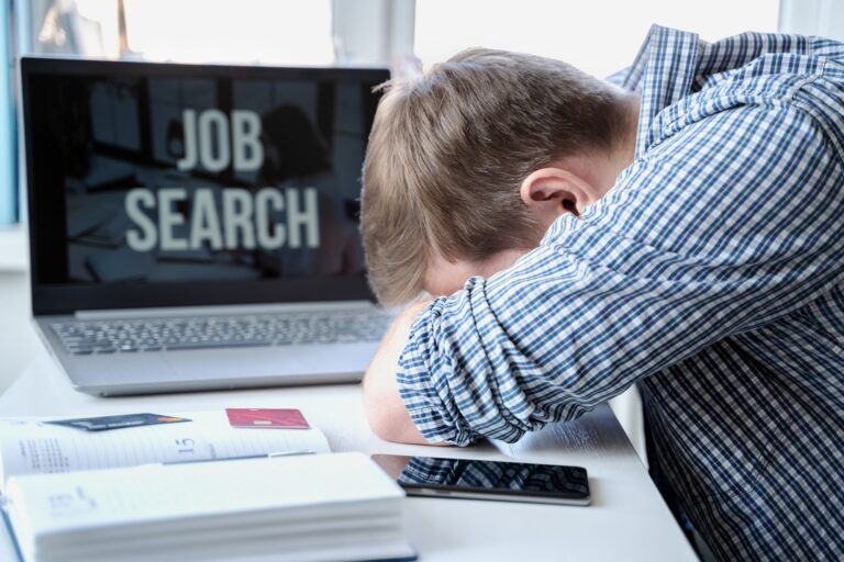 Man lies face down on table next to laptop. Looking for remote work. Unemployment,crisis